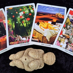 Puede incluir: Cuatro cartas de tarot con la imagen de la carta de los Enamorados, cada una con un estilo de collage diferente. Las cartas est&aacute;n dispuestas en semic&iacute;rculo con una peque&ntilde;a escultura de piedra beige redonda en el centro.