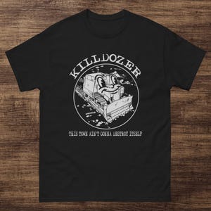 May include: Black t-shirt with a white graphic of a bulldozer with a smiling face inside a circle. The text "KILLDOZER" is above the image, and "THIS TOWN AIN'T GONNA DESTROY ITSELF" is below.