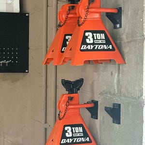 Può includere: Tre cavalletti di sollevamento Daytona 3 Ton Heavy Duty di colore arancione brillante montati a parete. Ogni cavalletto presenta una parte superiore nera regolabile, una catena metallica e un'etichetta nera con testo bianco 3 TON HEAVY DUTY DAYTONA.