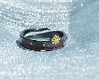 Könnte beinhalten: Ein schwarzer Ring mit einer roten Linie und einem goldenen Sternendesign. Der Ring ist mit kleinen klaren Steinen besetzt.