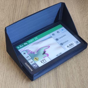 Puede incluir: Un dispositivo de navegación GPS negro con un parasol. La pantalla muestra un mapa con una ruta, la velocidad y la hora de llegada. El texto en la pantalla dice "6.3mi HWY 28", "27 mph Speed", "US 129", "Topographic", "BirdsEye" y "4:08 Arrival".