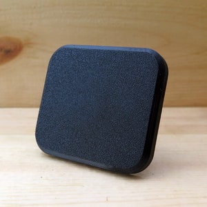 May include: A black square-shaped object with a textured surface. The object is made of a hard material and has rounded edges.