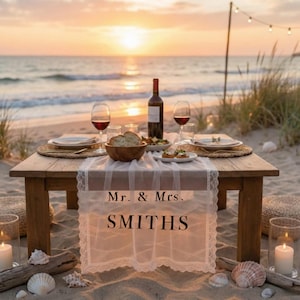 Peut inclure: Une table en bois dressée pour un pique-nique romantique sur la plage au coucher du soleil. La table est ornée d'assiettes, de verres à vin, d'une bouteille de vin et d'un centre de table avec du pain et de la nourriture. Un chemin de table en dentelle blanche affiche le texte "Mr. & Mrs. SMITHS".