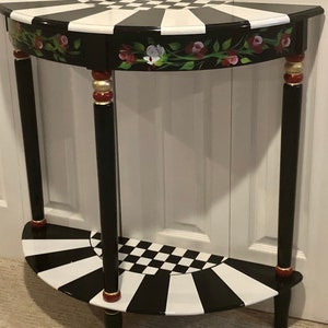 May include: A black and white half-moon table with a checkerboard pattern and floral accents. The table has two tiers and gold accents on the legs.