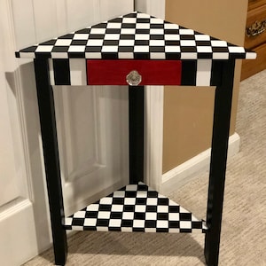 May include: A black and white checkered corner table with a red drawer and a crystal knob. The table has a lower shelf that is also checkered.