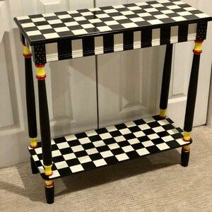 May include: A black and white checkered console table with a yellow and red trim on the legs. The table has a shelf and is made of wood.