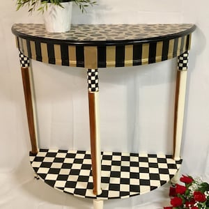 May include: A half-round table with a black and gold striped top, a black and white checkerboard bottom shelf, and white legs with black and gold accents.