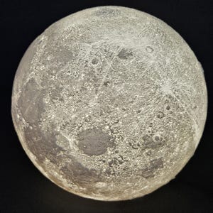 May include: A white moon lamp with a detailed surface texture resembling the moon's craters.
