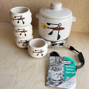 May include: A vintage white West Bend buffet patio server set. The set includes a lidded pot, four small bowls, and a booklet. Each piece features a design of a yellow fork and black spoon. The server sits on a chrome base with a black power cord.