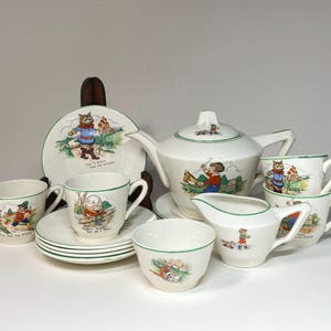 May include: A vintage children's tea set with a white background and green trim. The teapot, cups, saucers, and creamer feature colorful illustrations of children and animals. The set includes the text "Now We're Ready Now We're Late", "Happy Daddy Sat on a Wall", "We Two Are Friends", "Come Come Come", and "Little Bo Peep".