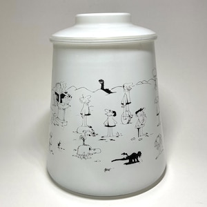 May include: White ceramic canister with a lid, decorated with black cartoon figures. The figures are in various poses, some standing, some lying down, and some playing musical instruments. The canister has a cylindrical shape.