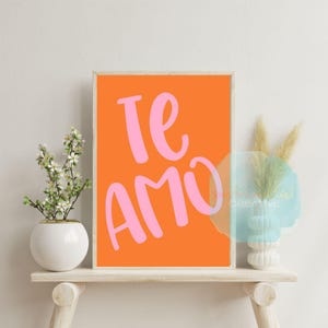 Op de afbeelding: Een ingelijst afdruk met een oranje achtergrond en de woorden "Te Amo" in roze letters.
