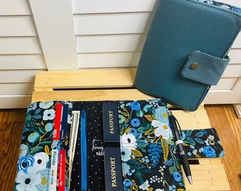 May include: A black passport holder with a floral pattern and a zipper closure. The holder has two clear plastic pockets for credit cards and a zippered pocket for cash. The holder also has two slots for passports. The holder is open and there are credit cards, cash, and passports inside.