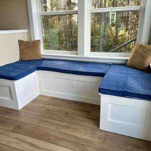 Può includere: Una panca di finestra bianca con cuscini blu e cuscini marroni. La panca è integrata in un muro e ha una cornice bianca.