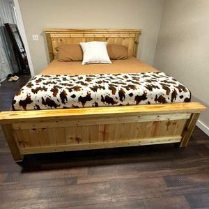 Könnte beinhalten: Ein Holzbettgestell mit einer braunen und weißen Kuhfelldecke. Das Bettgestell ist aus Naturholz mit rustikalem Finish.