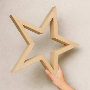 Può includere: Una stella di legno color chiaro con un design a cinque punte. La stella è tenuta da una mano su uno sfondo neutro. I bordi della stella sono smussati e la venatura del legno è visibile.
