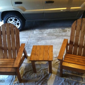 May include: Two wooden Adirondack chairs and a small square side table. The chairs have a slatted back and armrests. The furniture is made of stained wood and is suitable for outdoor use.