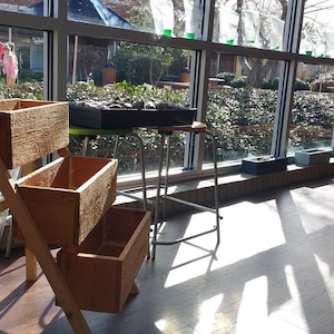 Peut inclure: Un bac &agrave; plantes en bois &agrave; trois niveaux avec trois bo&icirc;tes rectangulaires. La jardini&egrave;re est plac&eacute;e pr&egrave;s d'une grande fen&ecirc;tre, avec la lumi&egrave;re du soleil qui entre. Un panneau est visible en arri&egrave;re-plan. D'autres jardini&egrave;res sont sur un tabouret et un rebord de fen&ecirc;tre.