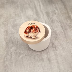 A wooden lid with a picture of a rabbit on it, placed on a white ceramic container.