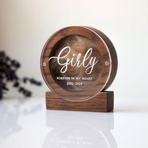 K&ouml;nnte beinhalten: Eine runde Holz-Erinnerungskiste mit einem durchsichtigen Deckel, die eine Haarstr&auml;hne enth&auml;lt. Die Box tr&auml;gt die Aufschrift "Girly Forever in my Heart 2002-2024" auf der Vorderseite.