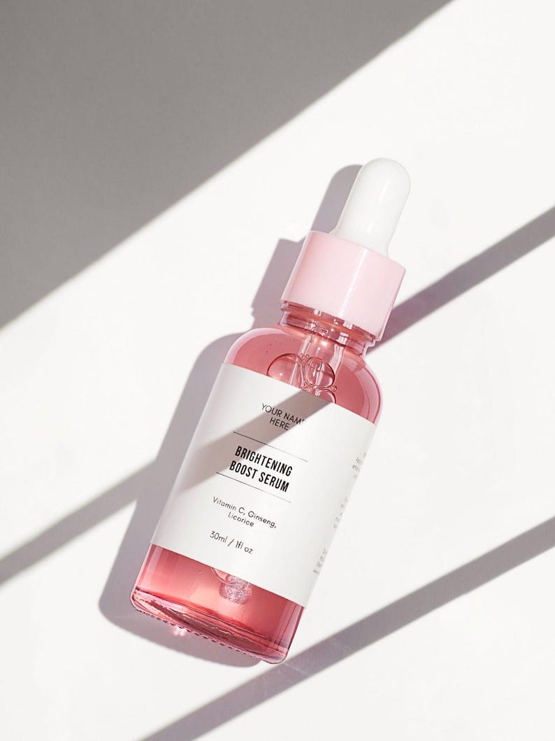 Pu&ograve; includere: Una bottiglia di vetro trasparente con un contagocce rosa riempita di un liquido rosa. La bottiglia ha un'etichetta bianca con il testo "BRIGHTENING BOOST SERUM" e "Vitamin C, Ginseng, Licorice" e "30ml / 1fl oz".