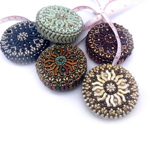 May include: Five beaded measuring tapes in different colors and patterns. The tapes are round and have a sunburst design. The colors include green, black, brown, purple, and white.