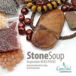 May include: An assortment of StoneSoup Inspiration Bead Packs featuring hand-cut cabs. The image displays various beads in shades of brown, red, and yellow, including faceted beads, round beads, and small seed beads. A large, oval-shaped stone cabochon is the focal point.