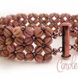 May include: A pink and brown beaded bracelet with a copper clasp. The bracelet is made with small, round beads that are arranged in a pattern. The clasp is a simple, rectangular design.