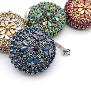 May include: Four beaded measuring tapes with different colored beads and designs. The tapes are in shades of gold, teal, purple, and blue.