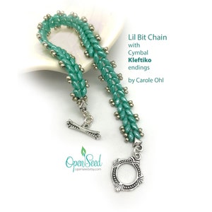 May include: A teal green beaded bracelet with silver accents and a silver clasp. The bracelet is called "Lil Bit Chain with Cymbal Kleftiko endings" by Carole Ohl.