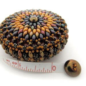 May include: A beaded measuring tape with a colorful, circular design. The tape is white with red markings and the numbers 1, 60, and 1 are visible.