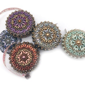 May include: Five beaded round measuring tapes in different colors, including purple, silver, green, and orange. The tapes are on a white background.