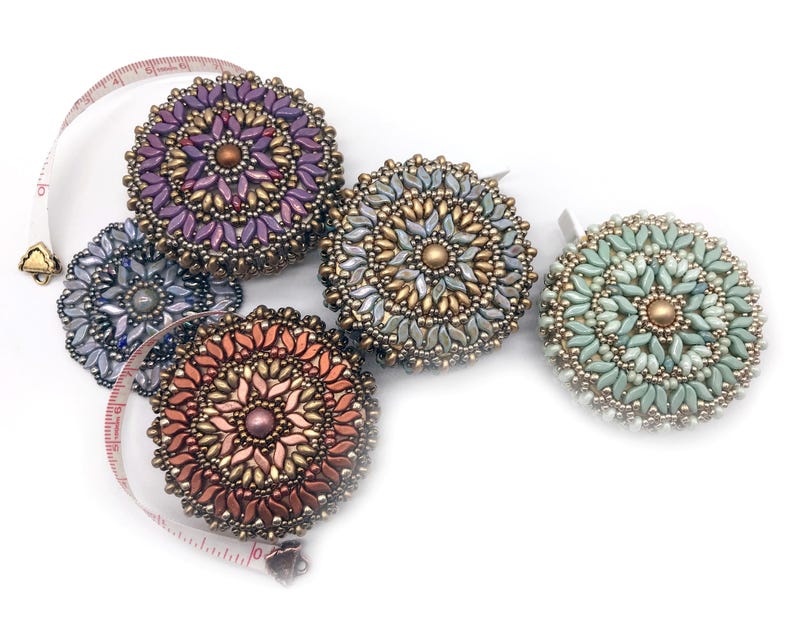 May include: Five beaded round measuring tapes in different colors, including purple, silver, green, and orange. The tapes are on a white background.