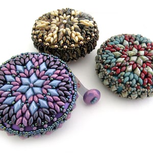 May include: Three beaded measuring tapes with different colored designs. The tape on the left has a purple, blue, and pink design. The tape in the middle has a brown, white, and gold design. The tape on the right has a red, blue, and green design.