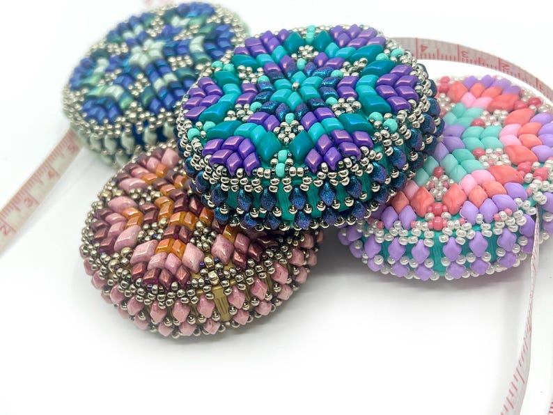 May include: Four colorful beaded tape measures with geometric patterns in shades of pink, purple, blue, and turquoise.