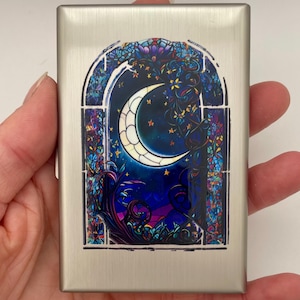 May include: A rectangular brushed silver metal case featuring a centered graphic print of a crescent moon set within an arched window frame. The design incorporates deep blue, purple, and teal tones with intricate floral and star patterns.