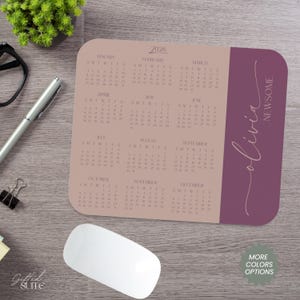 May include: A personalized mousepad featuring a 2026 calendar in a neutral color scheme. The design includes the name "Olivia Newsome" in a script font and a "More Colors Options" button. The mousepad is rectangular with rounded corners.