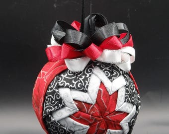 May include: A red, white, and black fabric Christmas ornament with a starburst design. The ornament is decorated with a black and white ribbon bow.
