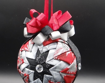 May include: A red, black, and silver fabric Christmas ornament with a starburst design and a rhinestone in the center. The ornament is hanging from a red ribbon.