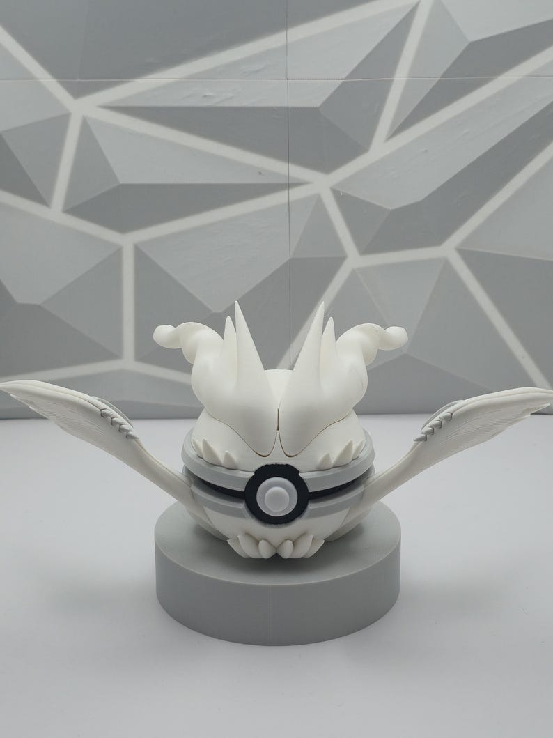 May include: A white spherical figure with pointed, wing-like appendages extending from the sides and a central circular black and white button detail. The object features sharp, flame-like protrusions on top and rests on a solid gray cylindrical base.