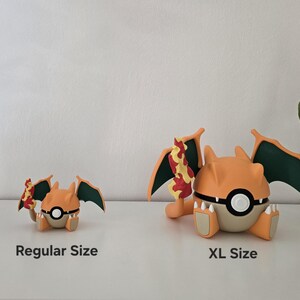 May include: Two orange and tan dragon-like figurines with dark green wings and a flame-tipped tail. The smaller figure is labeled Regular Size and the larger figure is labeled XL Size. Both figures feature a central white and black circular emblem.
