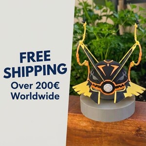 May include: A spherical figurine featuring a black and orange geometric pattern with a central white circular element, two tall yellow antennae-like structures extending upwards, and a yellow base, all mounted on a solid gray cylindrical stand.