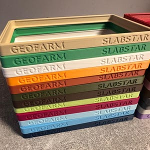 Pu&ograve; includere: Una pila di contenitori rettangolari colorati con i testi "GEOFARM" e "SLABSTAR" stampati sopra. I contenitori sono in vari colori, tra cui beige, verde, bianco, arancione, marrone e blu.