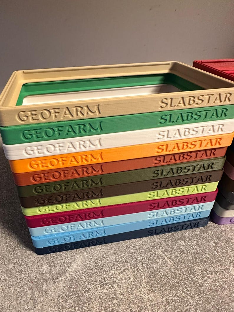 Pu&ograve; includere: Una pila di contenitori rettangolari colorati con i testi "GEOFARM" e "SLABSTAR" stampati sopra. I contenitori sono in vari colori, tra cui beige, verde, bianco, arancione, marrone e blu.