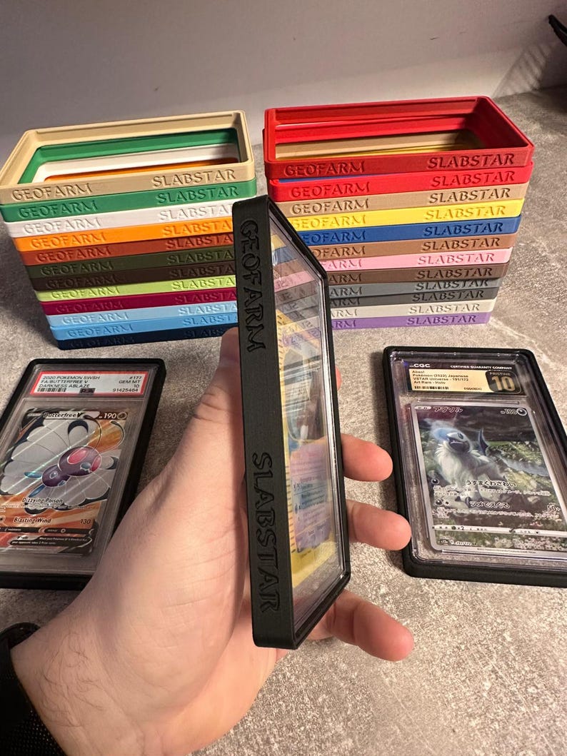 Pu&ograve; includere: Una pila di scatole colorate per la conservazione di carte con le scritte "GEOFARM" e "SLABSTAR". Sono visibili due custodie per carte classificate, una con una carta Pok&eacute;mon.