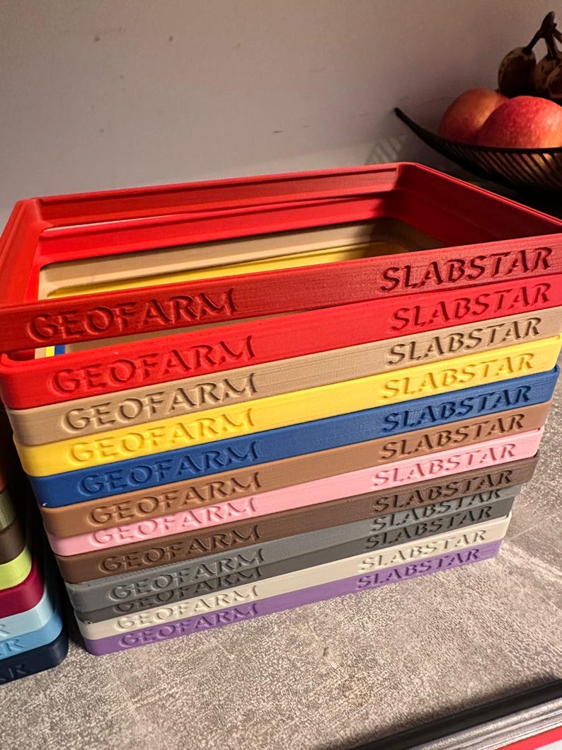 Pu&ograve; includere: Una pila di vassoi rettangolari colorati con la scritta "GEOFARM" e "SLABSTAR" stampata sopra. I vassoi sono di vari colori, tra cui rosso, giallo, blu e marrone. I vassoi sono impilati uno sopra l'altro.