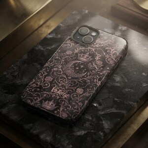May include: A black smartphone case featuring a rose gold filigree pattern of roses, vines, and crowns. A central crescent moon and star motif is visible, along with the text Valnty printed in a script font near the bottom of the case.