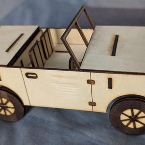 May include: A wooden toy car model with a removable top, a detailed interior, and four wheels. The car is made of light brown wood and has a simple design.