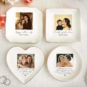 Puede incluir: Cuatro platos decorativos de cerámica blanca con borde dorado, cada uno con una fotografía. Los platos son cuadrados, redondos, en forma de corazón y cuadrados con bordes redondeados. Se imprime texto y fechas en los platos. También se ve un collar de perlas y anillos.