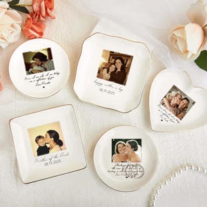 Puede incluir: Una colección de platos de cerámica personalizados en varias formas: redondos, cuadrados y en forma de corazón. Cada plato presenta una fotografía y texto personalizado con un borde dorado. Los platos están dispuestos sobre una superficie blanca con detalles florales.